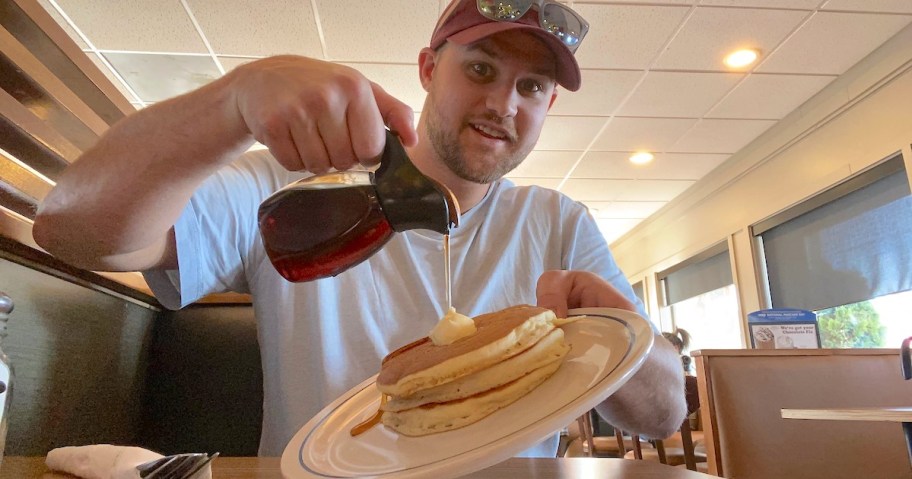 man holding a plate of pancakes with syrup