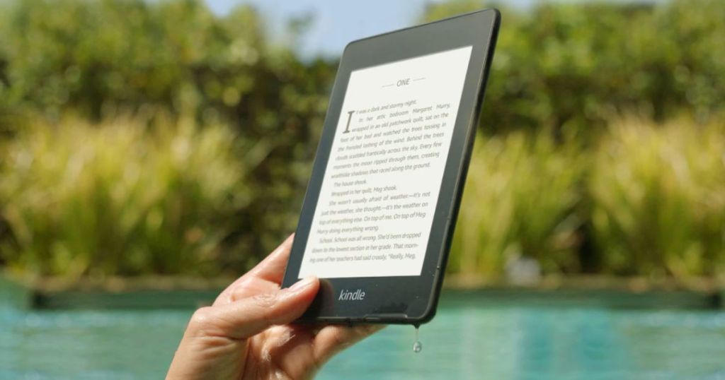 person reading book on kindle with trees and water in the background