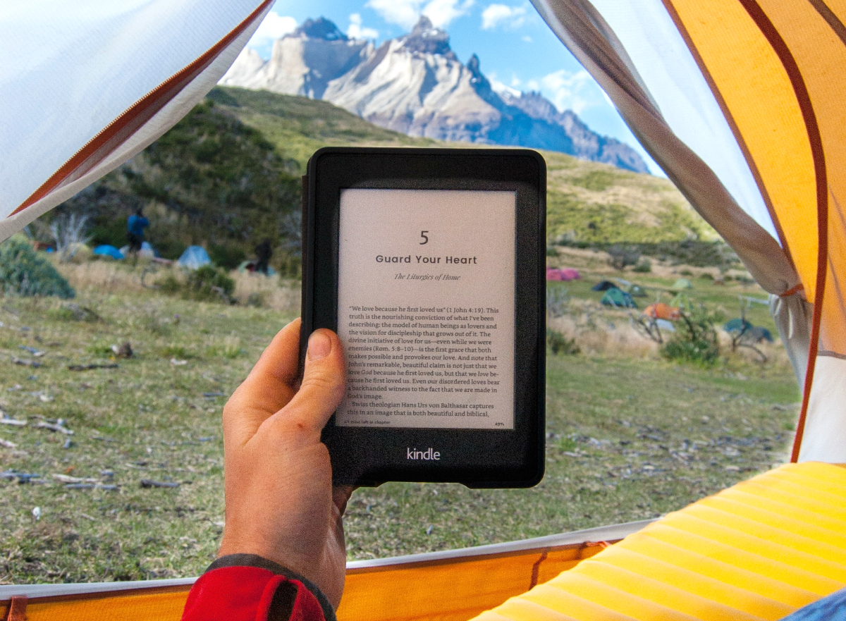 person reading Kindle from tent in mountains