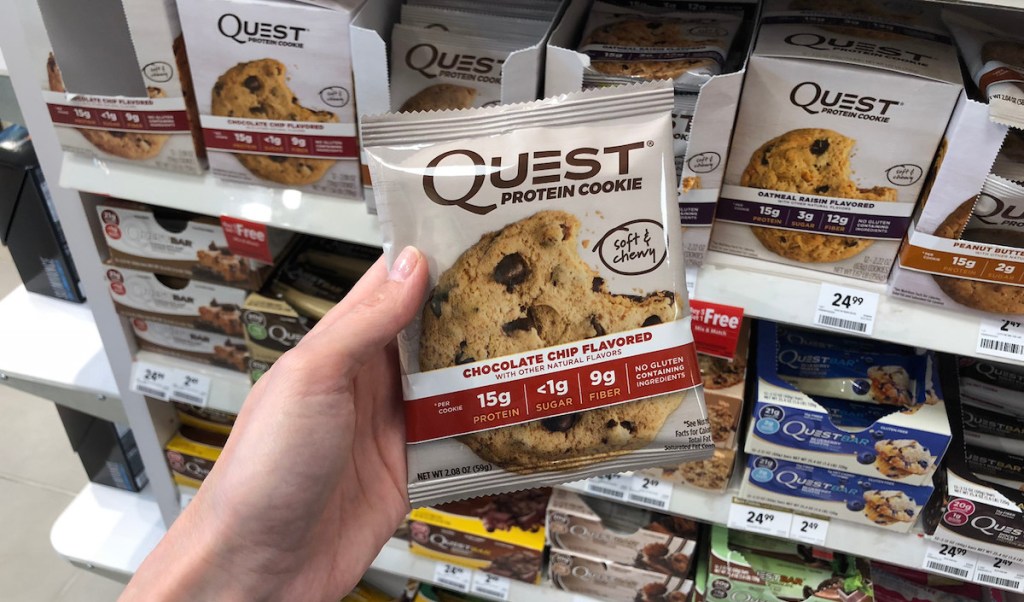 hand holding a quest chewy cookie in bag with other nutritional snacks in background