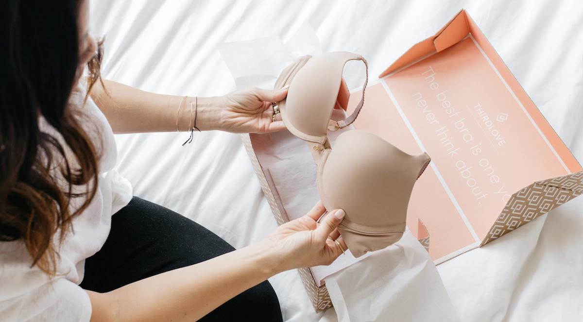 hands holding a nude colored bra with open orange third love box
