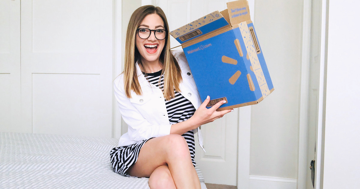 woman sitting on bed smiling holding a blue walmart box