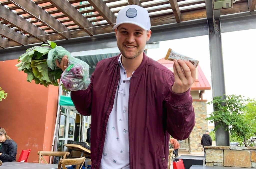 man holding snack bar and bag of beets in vegetable bag outside