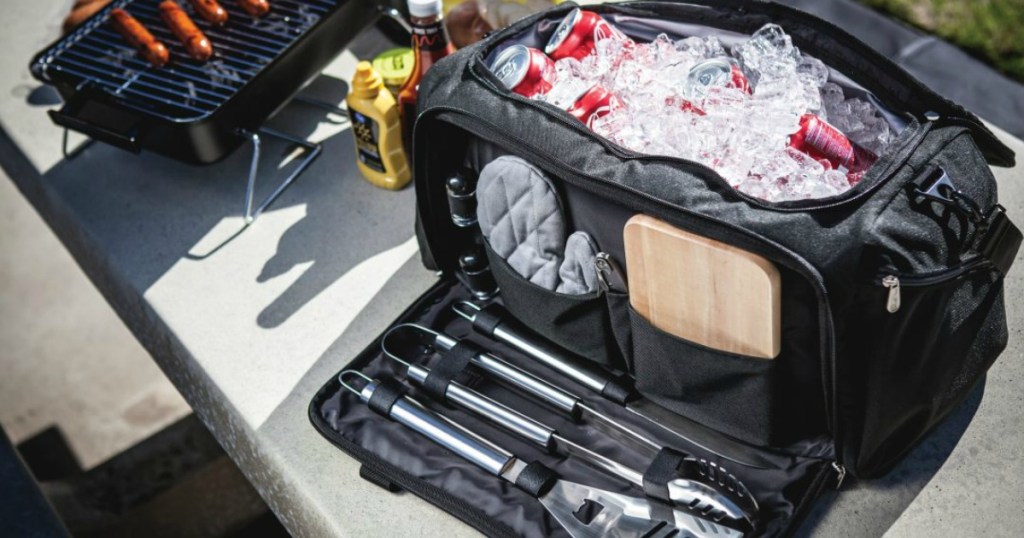 Black cooler duffel full of soda cans. Front pocket contains barbecue cooking accessories. 