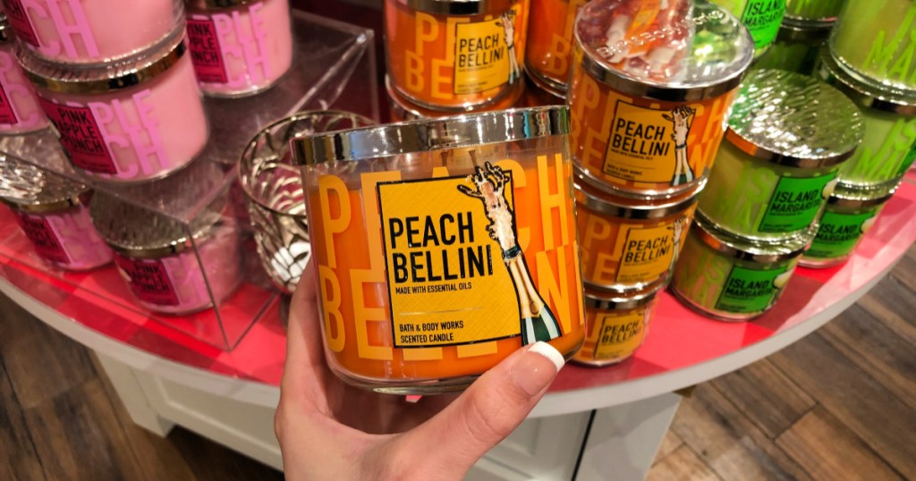 Bath & Body Works Peach Bellini 3 wick candle held in hand in store with various 3 wick candles in the background