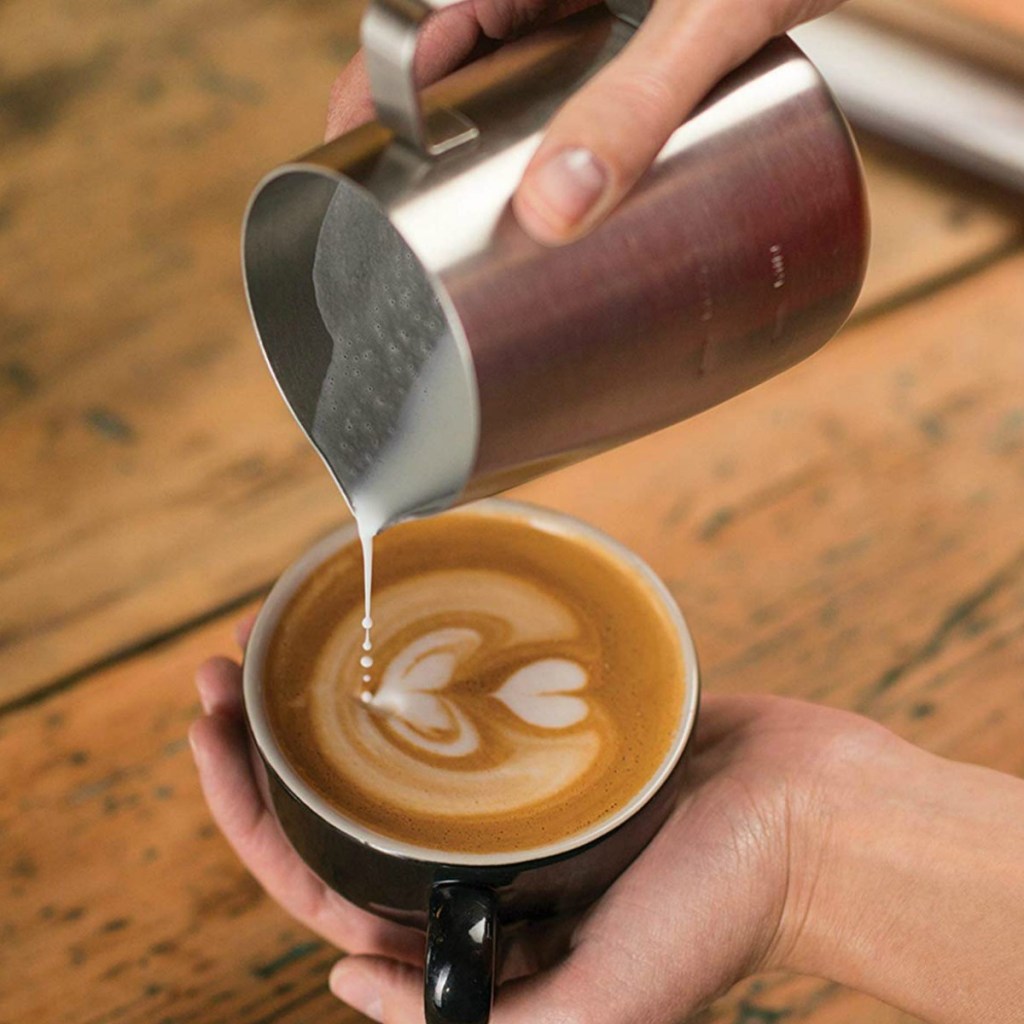 Stainless milk jug pouring frothed milk into coffee