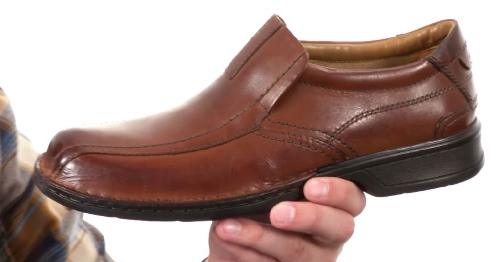 Man wearing plaid shirt holding CLARKS Men's Escalade Step in brown
