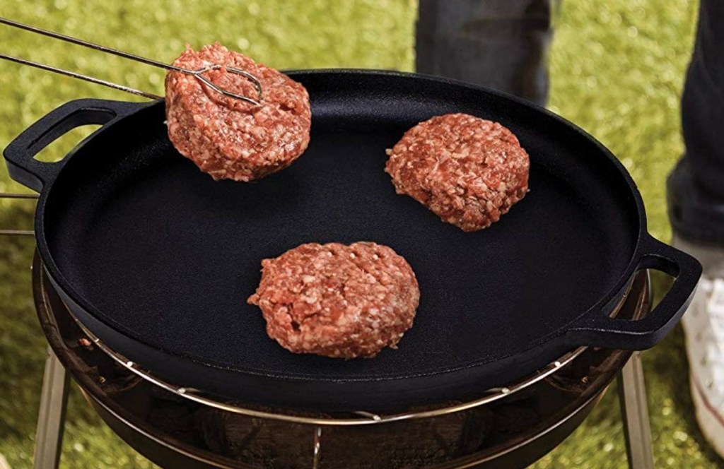 Flat cast iron pan on grill with three burger patties