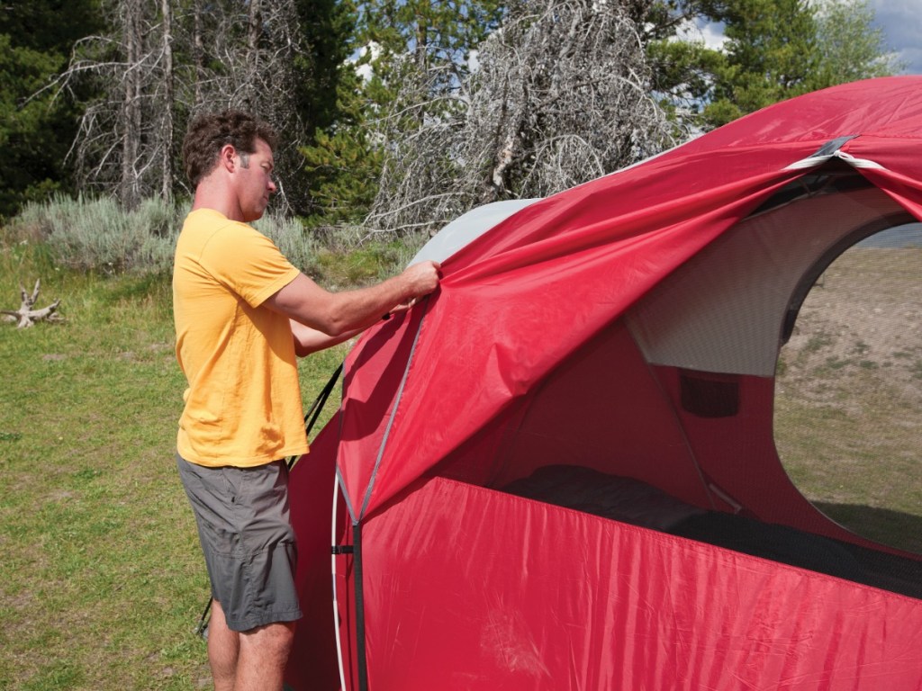 Man putting together a red Coleman tent