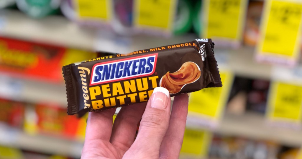 female hand holding up creamy snickers peanut butter candy bar at cvs