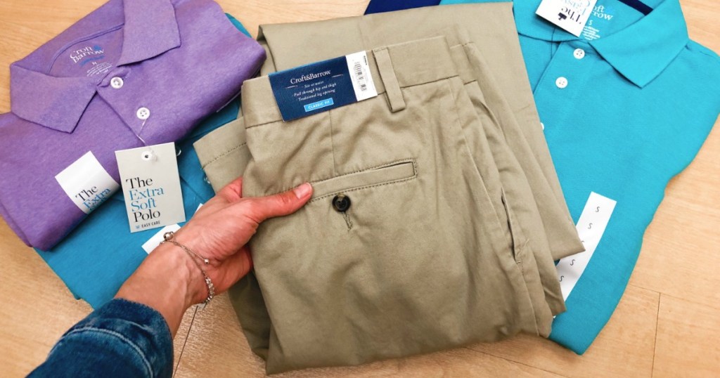 Men's Khaki pants being held by a woman in front of polo shirts at Kohl's