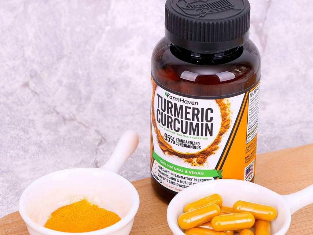 farmhaven tumeric curcumin bottle on table with bowl of powder and bowl of capsules