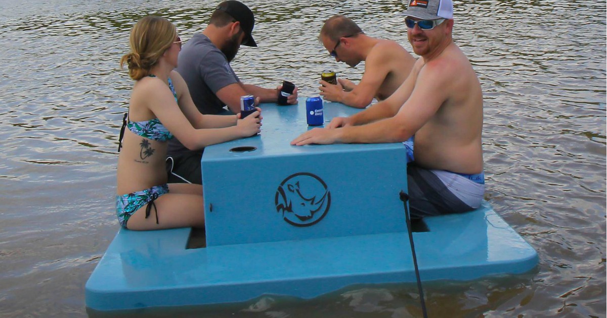 4 adults sitting on floating picnic table on water drinking beer