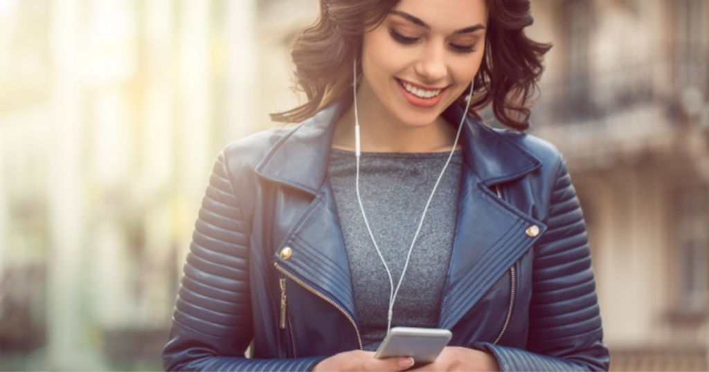 girl smiling and listen to mustic with headphones connected to her phone