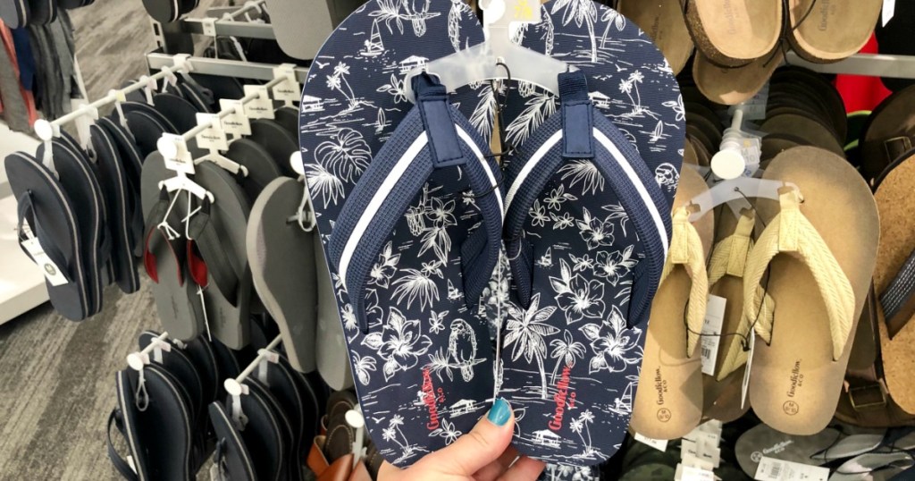 Blue flip flops with white tropical flowers held up in front of hanging summer shoe dispay 