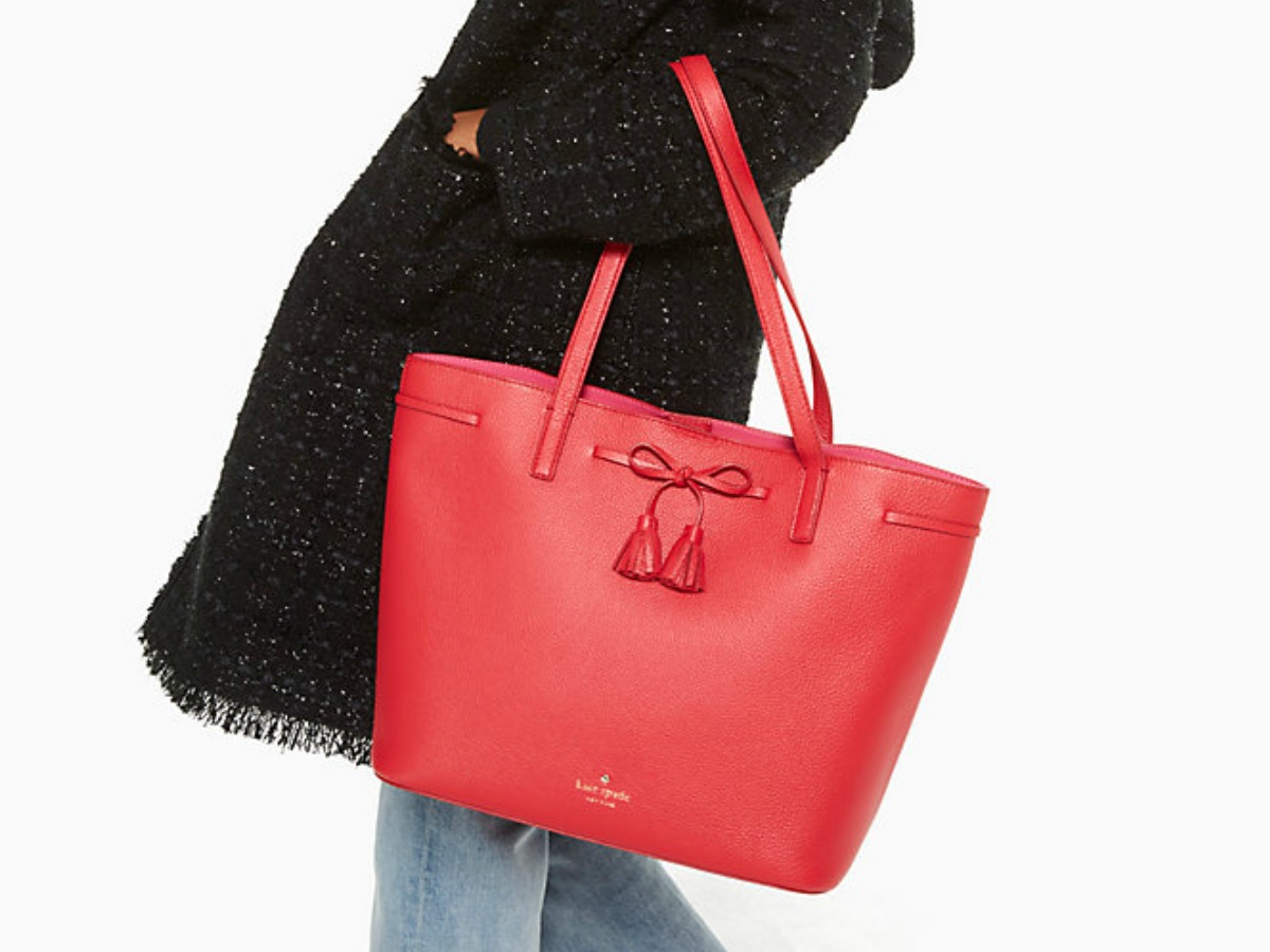lady in black trench coat holding large red Kate Spade tote