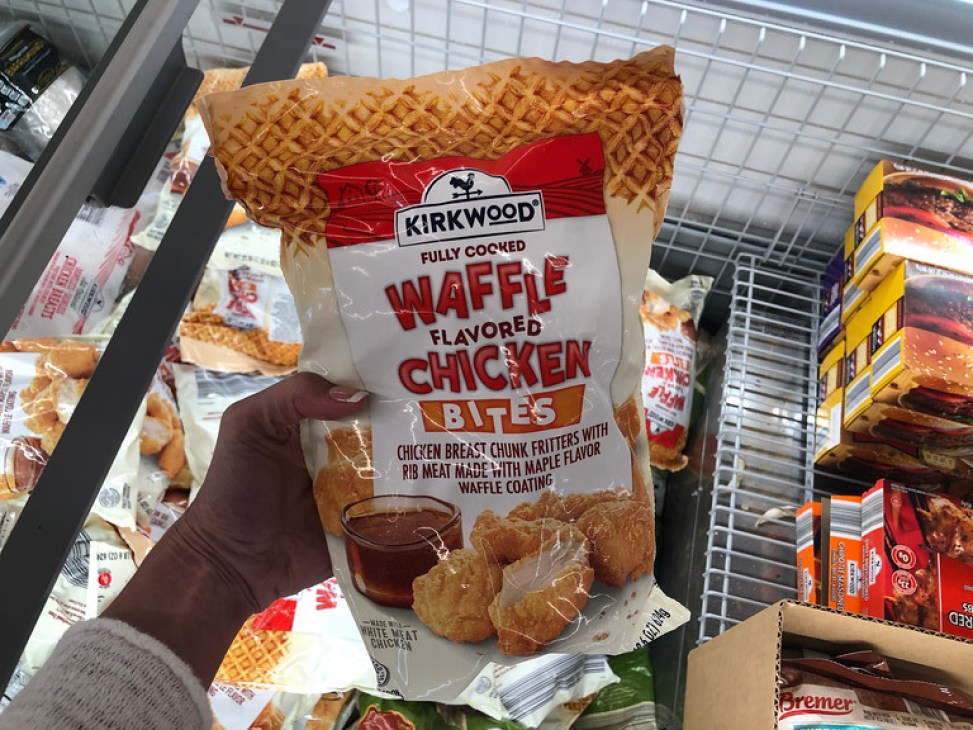 Woman holding Kirkwood Waffle Flavored Chicken Bites in ALDI freezer section