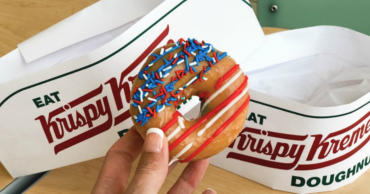 Hand holding Krispy Kreme Flag Doughnut in front of signature Krispy Kreme paper hats