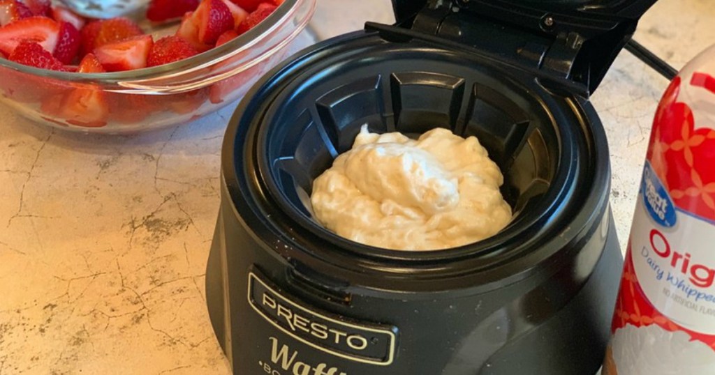 presto waffle bowl maker with batter inside of machine with strawberries and whipped cream