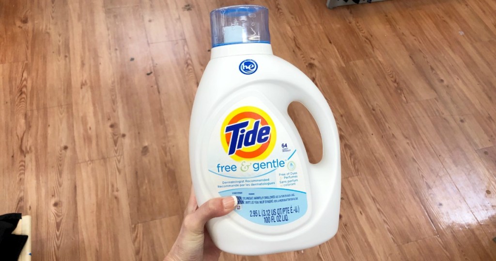 woman's hand holding Tide Free & Gentle detergent bottle above wood floor
