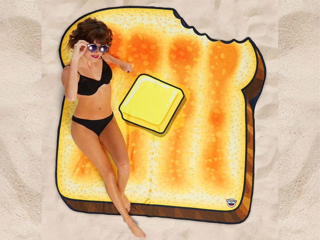 woman in black bathensuit laying on toast beach blanket on sand