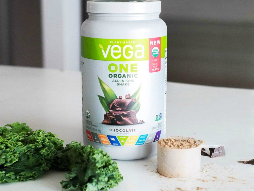 vega one chocolate protein powder on counter with lettuce and measuring cup of powder sitting next to it
