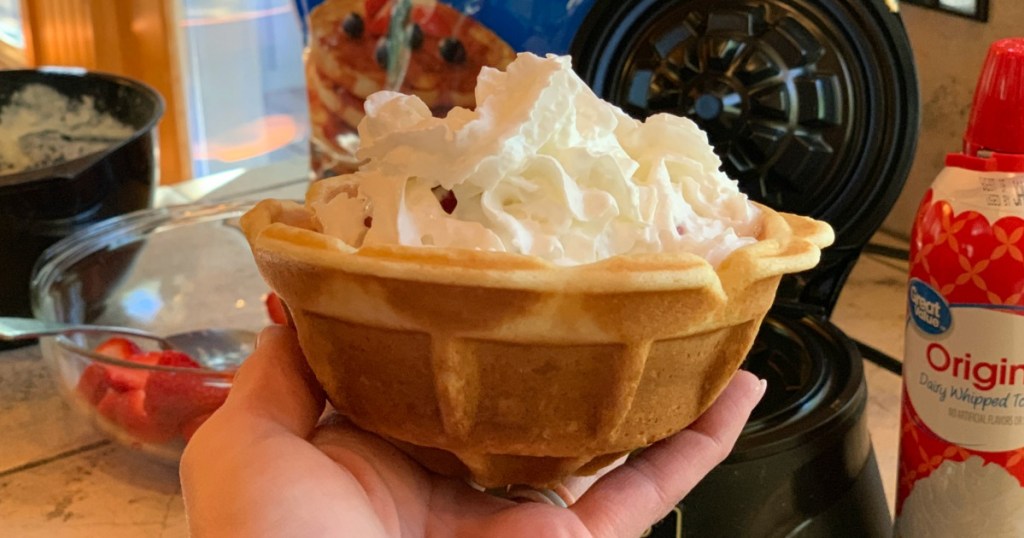 hand holding waffle bowl with whipped cream inside of it