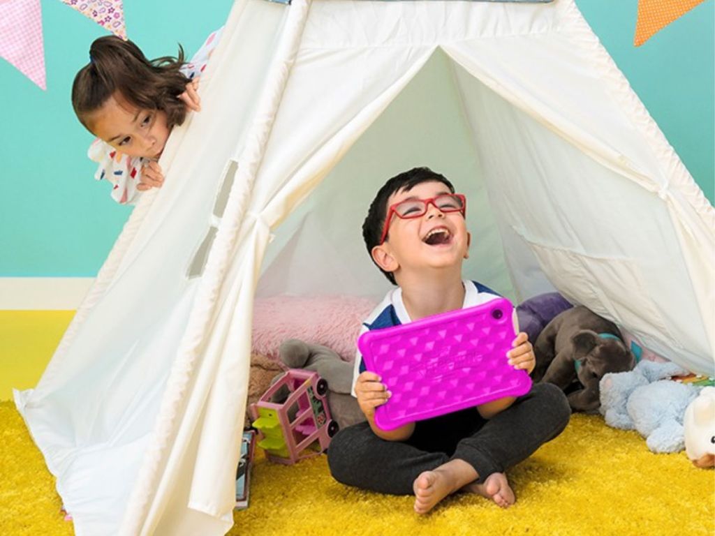 boy holding pink amazon kids fire table sitting in a white tent with girl peaking around the side