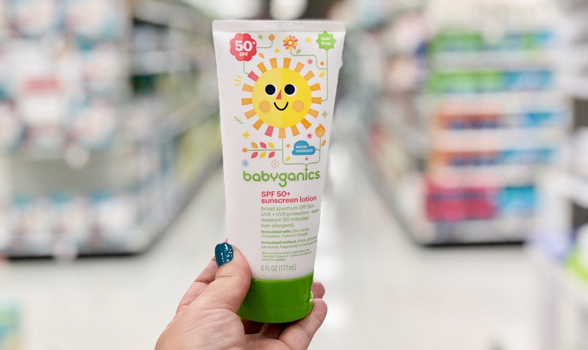 Hand holding a bottle of babyganics sunscreen with store shelves in background