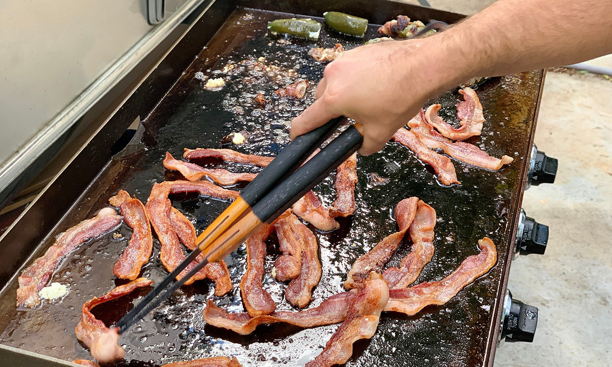 man cooking bacon on blackstone griddle