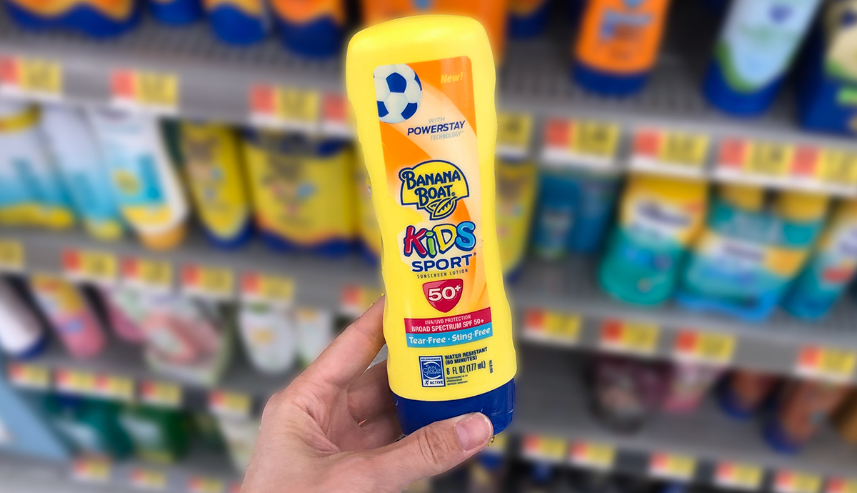 Hand holding a yellow bottle of kids sport banana boat sunscreen with store shelf in background