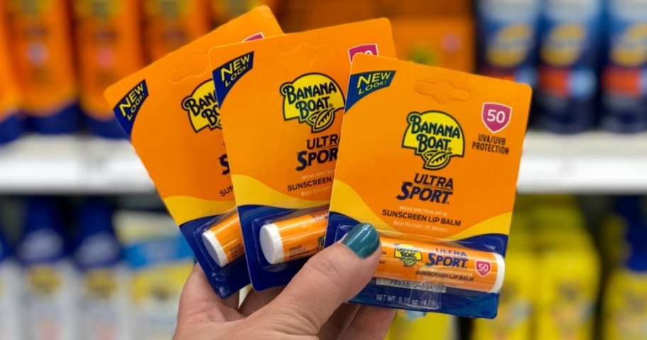 person holding three packages of banana boat sunscreen lip balm in store