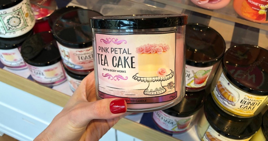 hand holding pink petal tea cake candle with various candles in background