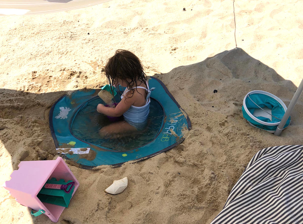 baby girl in blue pool in sand at beach