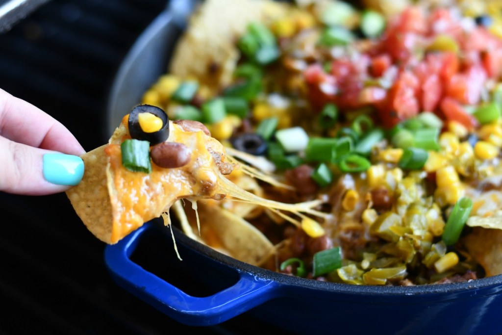 picking up a cheesy nacho from a skillet