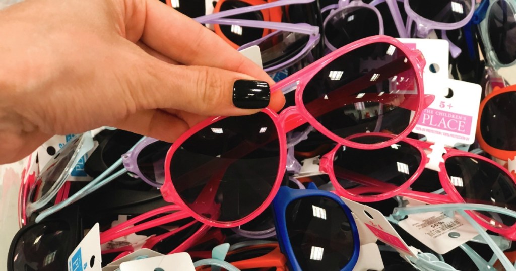hand holding pair of sunglasses over pile of sunglasses