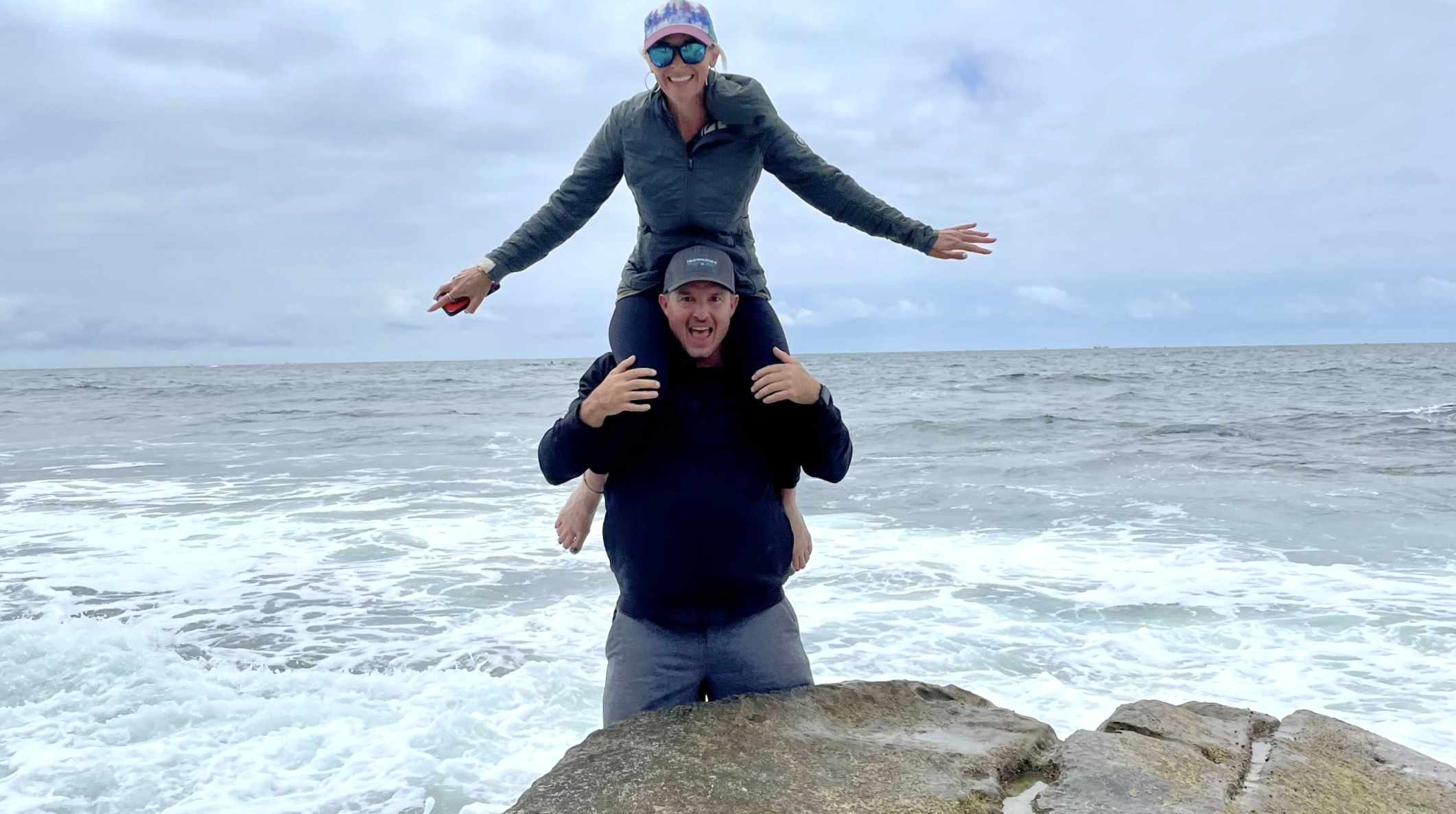 woman sitting on mans shoulders in the ocean enjoying cheap family vacations in san diego