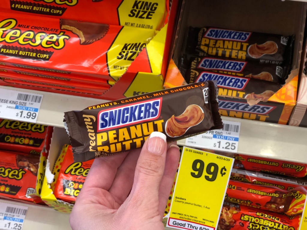 female hand holding up creamy snickers peanut butter candy bar at cvs in front of sale sign