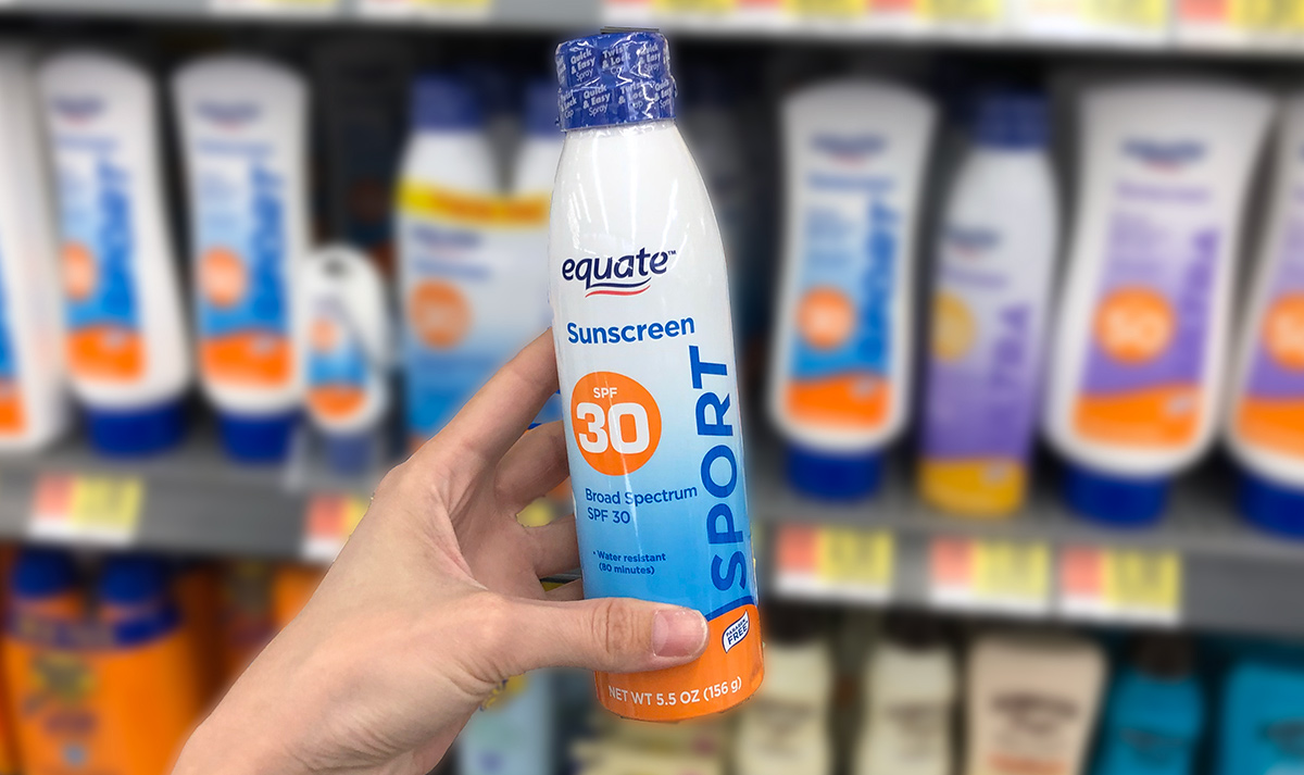 Hand holding a bottle of equate sunscreen spray with store shelf in background