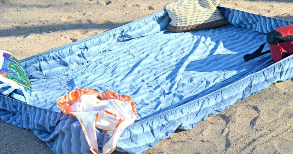 blue fitted sheet on sand with stuff in each corner