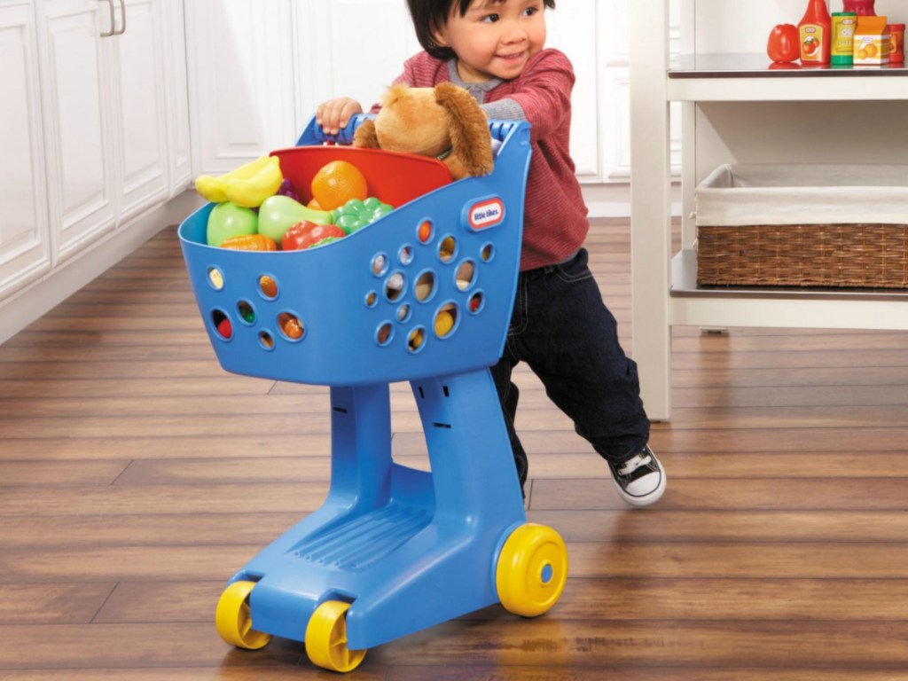 little boy pushing blue little tikes kids shopping cart filled with pretend food