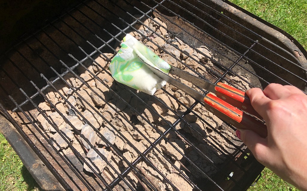 tongs with an oil soaked paper towel wiping down grill grates