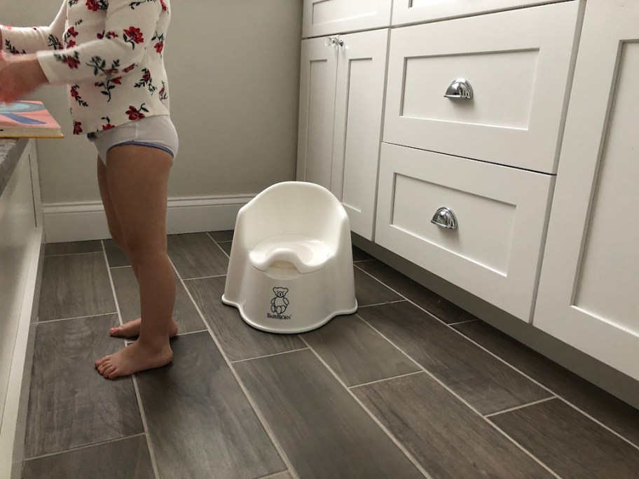 child standing in bathroom by potty seat 