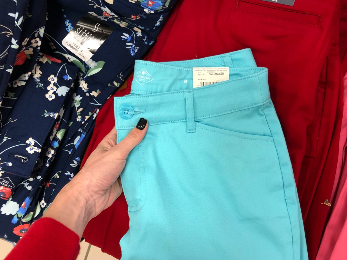 hand holding a pair of sky blue jcpenney capris above other clothes on display in store