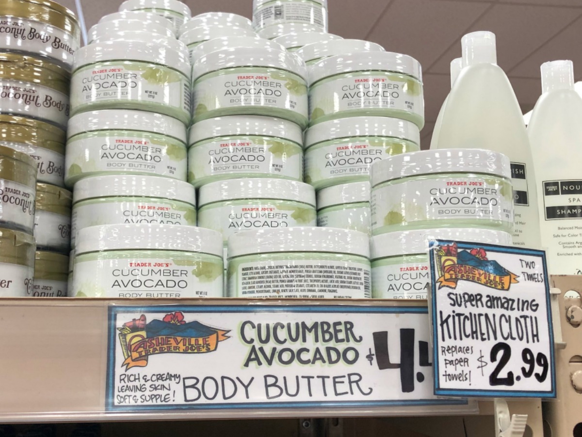 trader joe's cucumber avocado body butter jars stacked on a store shelf with promotional sign