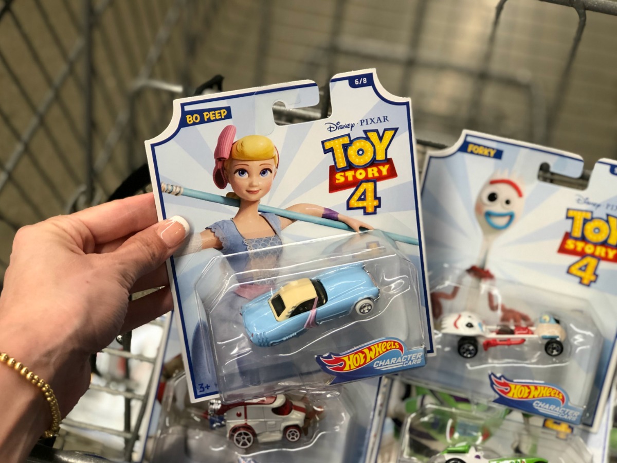 hand holding a package with a kids toy car in front of shopping cart