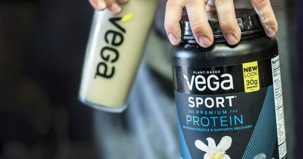man holding vega cup with shake in one hand and jar of vega sport powder in the other hand