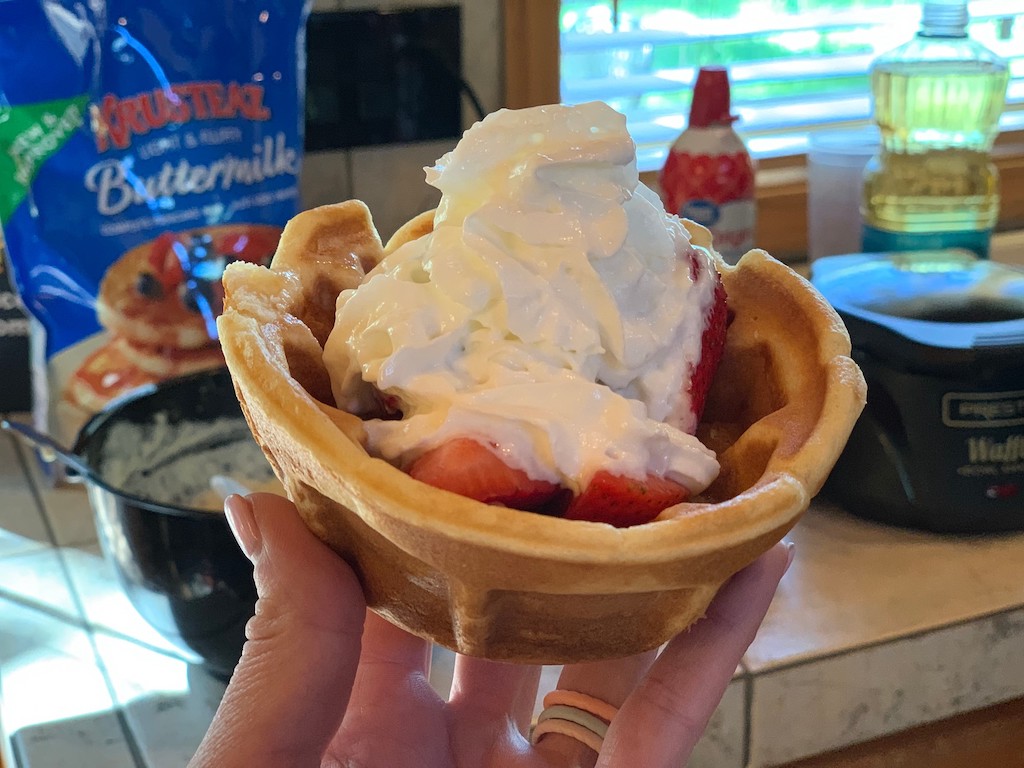 holding waffle bowl with strawberries and whipped cream 