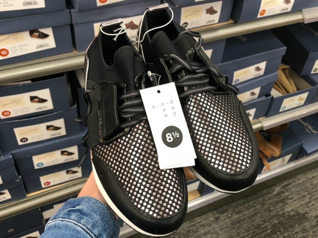 hand holding pair of black shoes in store by display