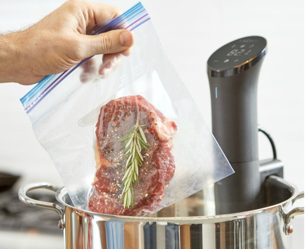 Hand holding a bag with steak next to an Anova sous vide